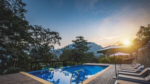 A wooden deck with a swimming pool, lounge chairs, and umbrellas.