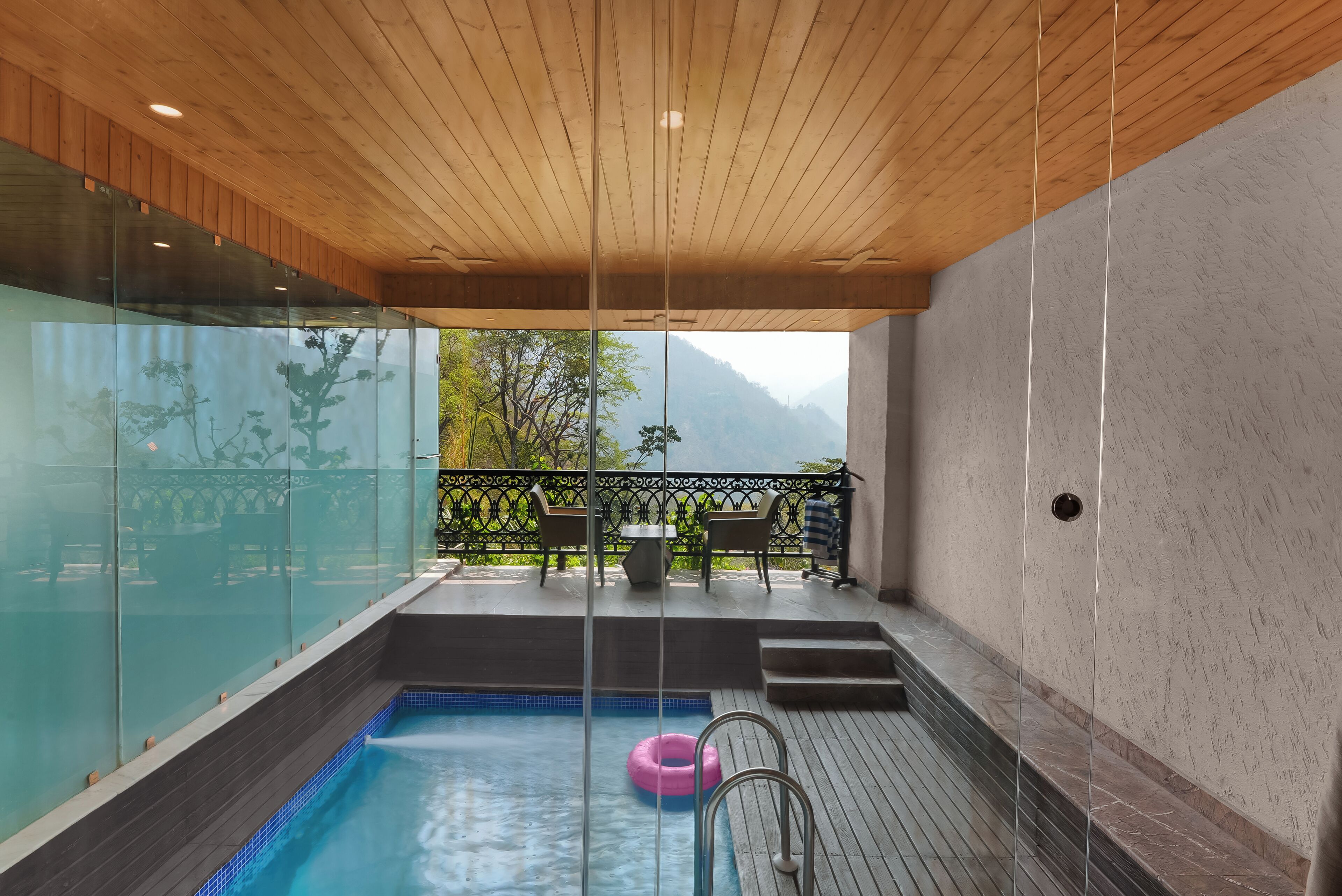 A modern indoor pool area with a wooden ceiling, glass walls, and a view of mountains.