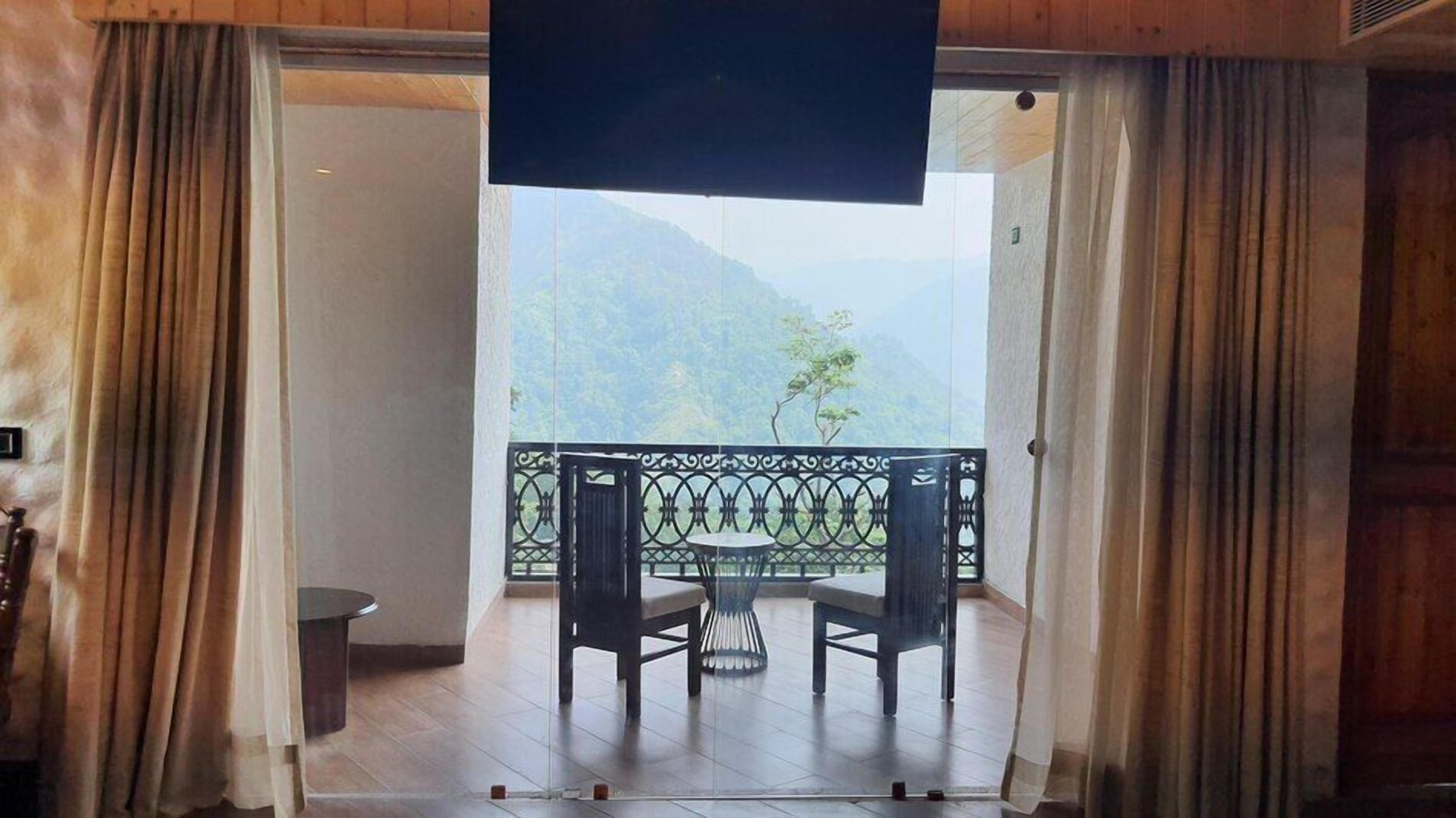 A room with a view of mountains, a balcony with a table and chairs, and a TV screen.