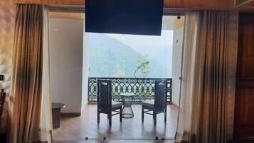 A room with a view of mountains, a balcony with a table and chairs, and a TV screen.