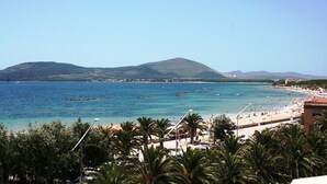 Escena costera con aguas azules cristalinas, una playa arenosa y una montaña al fondo.