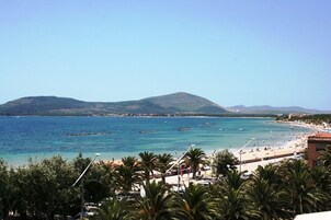 Paesaggio costiero con acque blu cristalline, spiaggia sabbiosa e una montagna sullo sfondo.