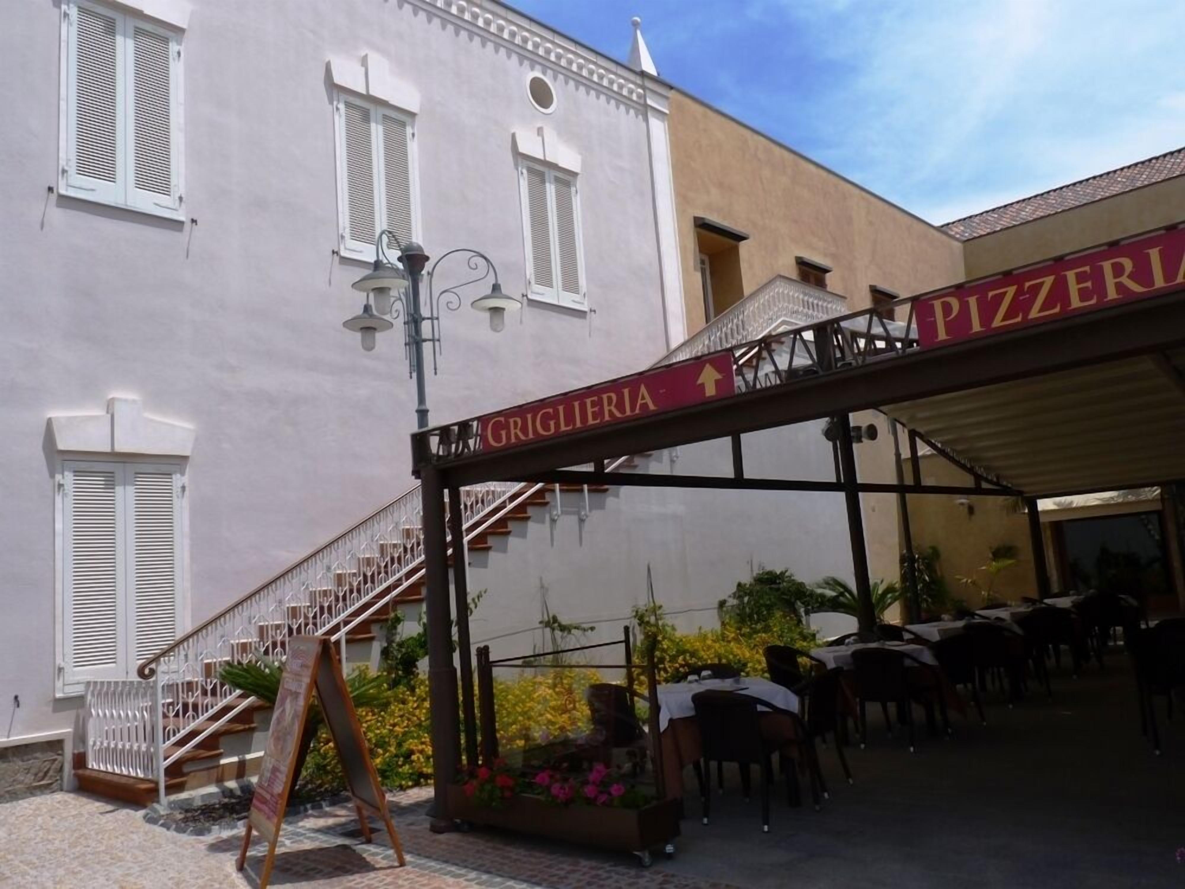Un bâtiment sur lequel on peut lire les inscriptions « PIZZERIA » et « GRIGLIERIA », ce qui indique qu’il s’agit d’un restaurant. Un escalier mène à un étage supérieur.