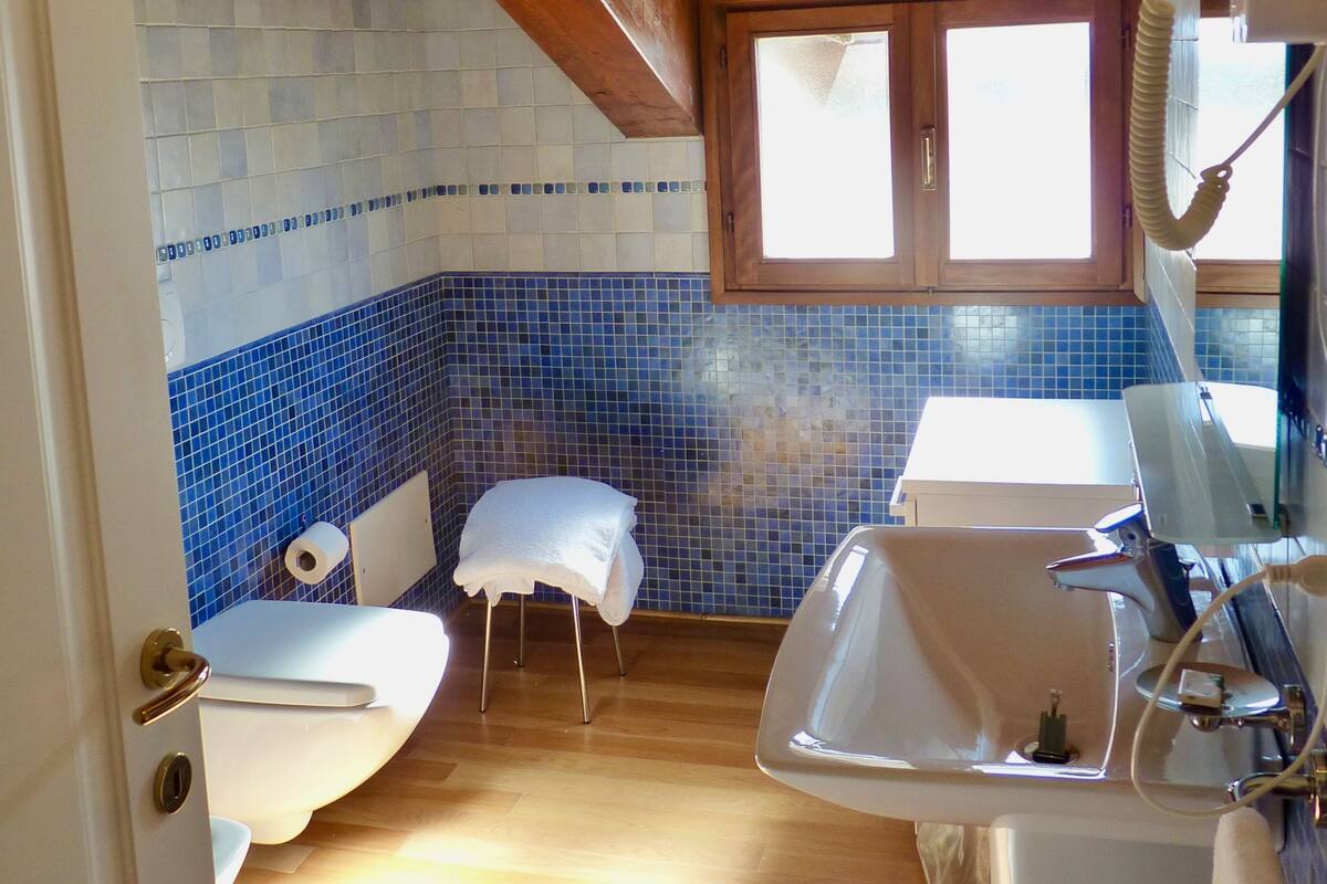 Un baño con techo de madera, pared con azulejos azules, inodoro, lavabo y bañera.