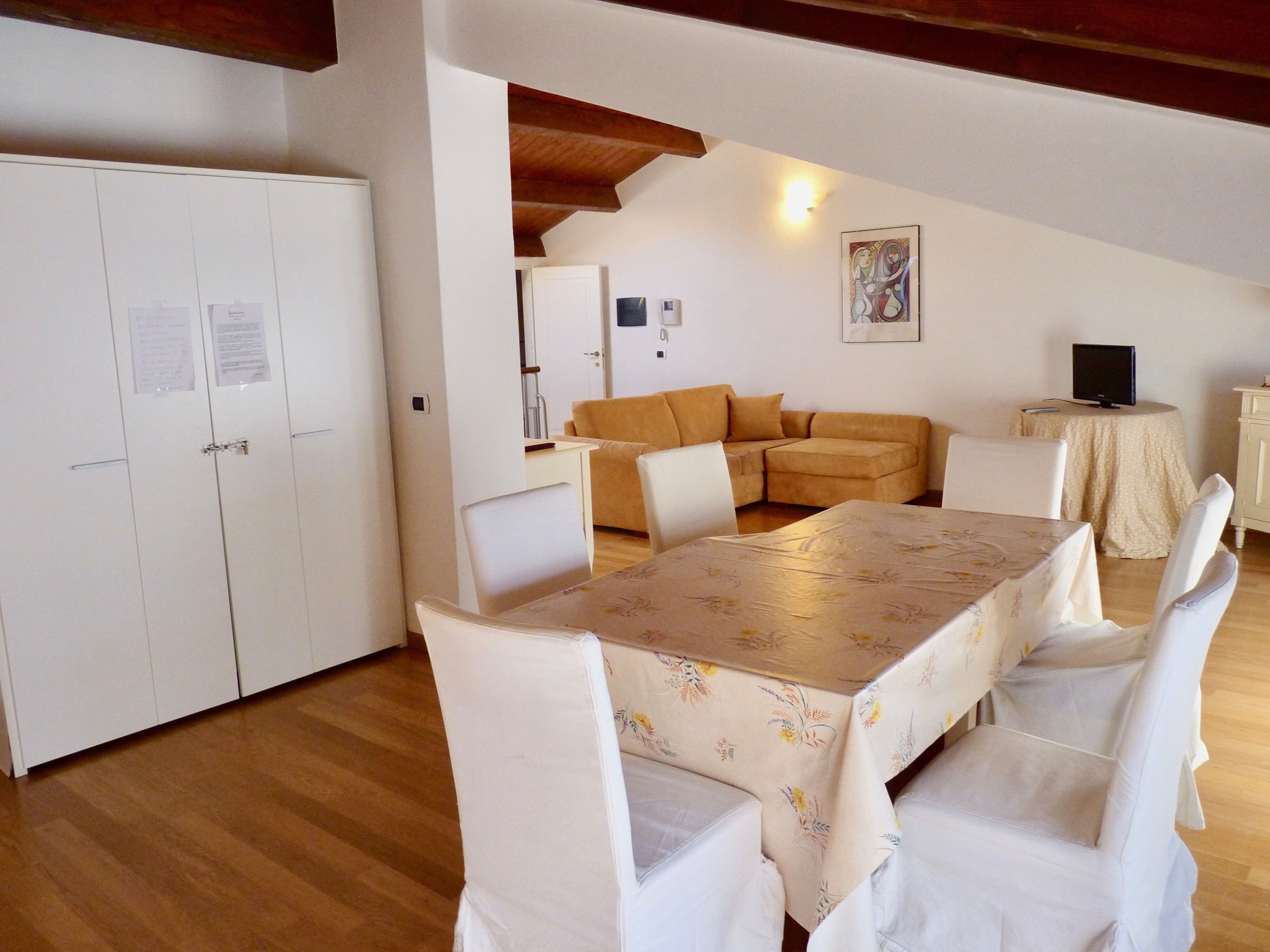 Un espacio habitable compacto con una mesa de comedor, sillas blancas, un sofá y un televisor sobre una mesita.