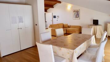 Un espacio habitable compacto con una mesa de comedor, sillas blancas, un sofá y un televisor sobre una mesita.