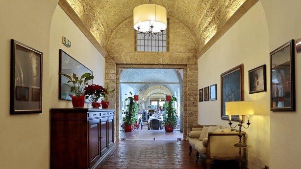 Un pasillo con piso de ladrillo, arcos de piedra y obras de arte enmarcadas en las paredes.