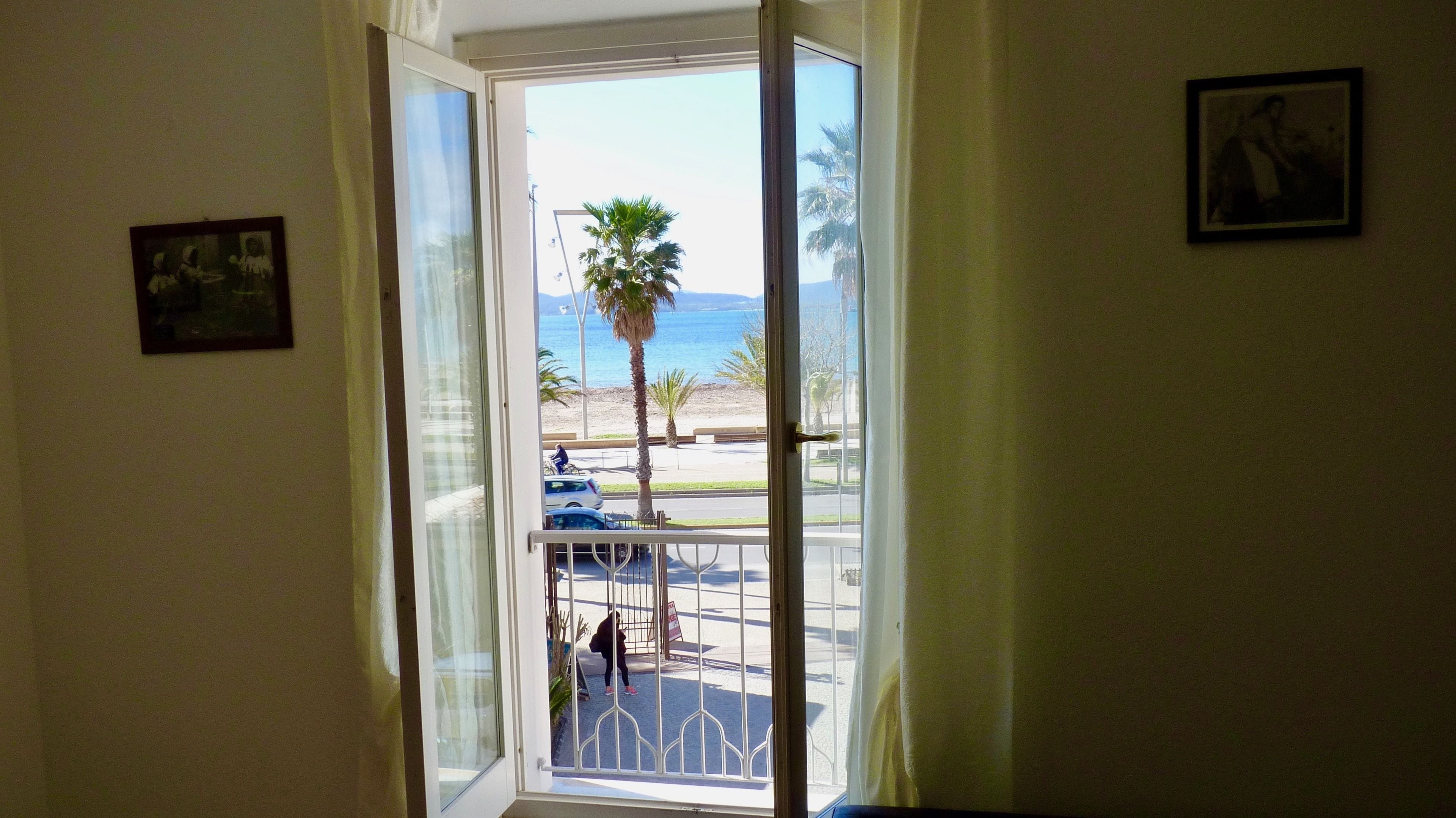 Una puerta que da a un balcón con vista a la playa y palmeras.