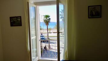 Una puerta que da a un balcón con vista a la playa y palmeras.