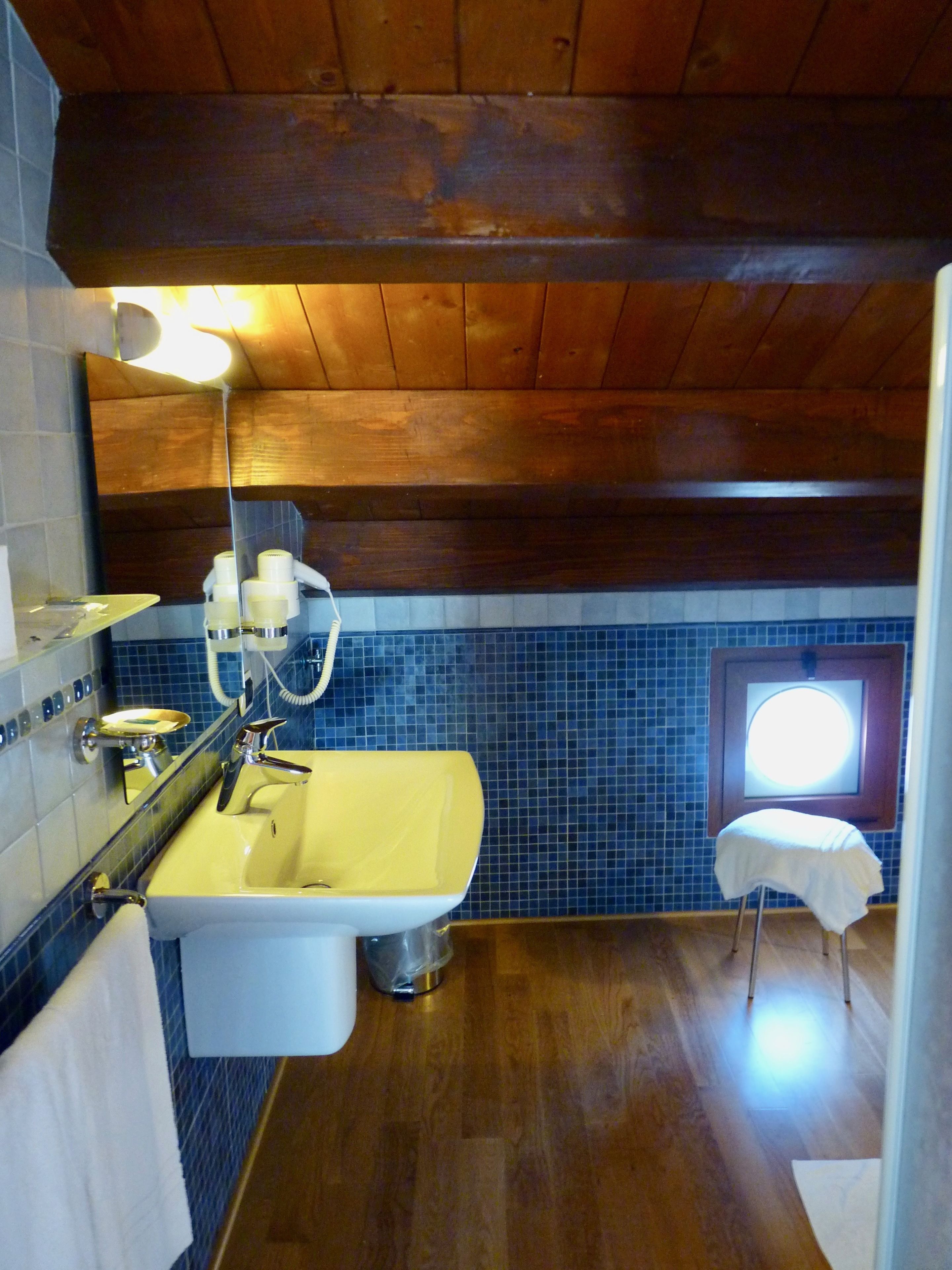 A bathroom with a wooden ceiling, a yellow sink, a mirror, and a window.
