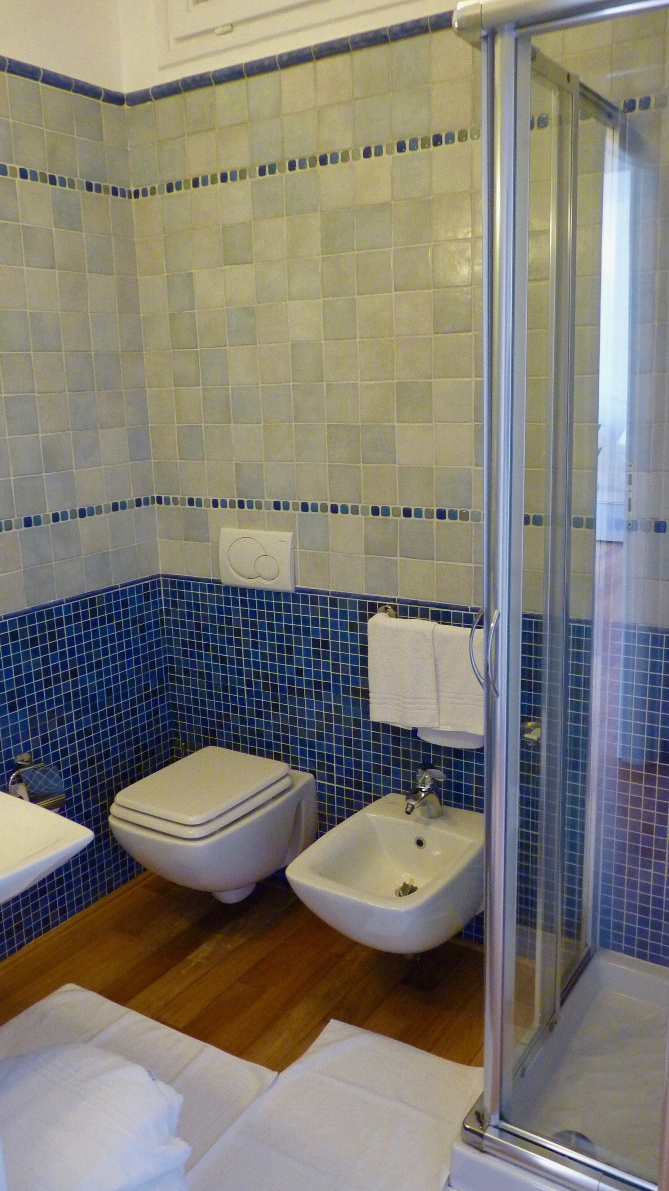 Un baño con inodoro, bidé, lavamanos y cabina de ducha con mampara de vidrio.