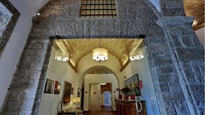 Un arco de piedra que da acceso a un pasillo con una araña y cuadros enmarcados.