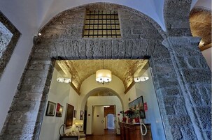 Un arco in pietra conduce a un corridoio con un lampadario e quadri appesi.
