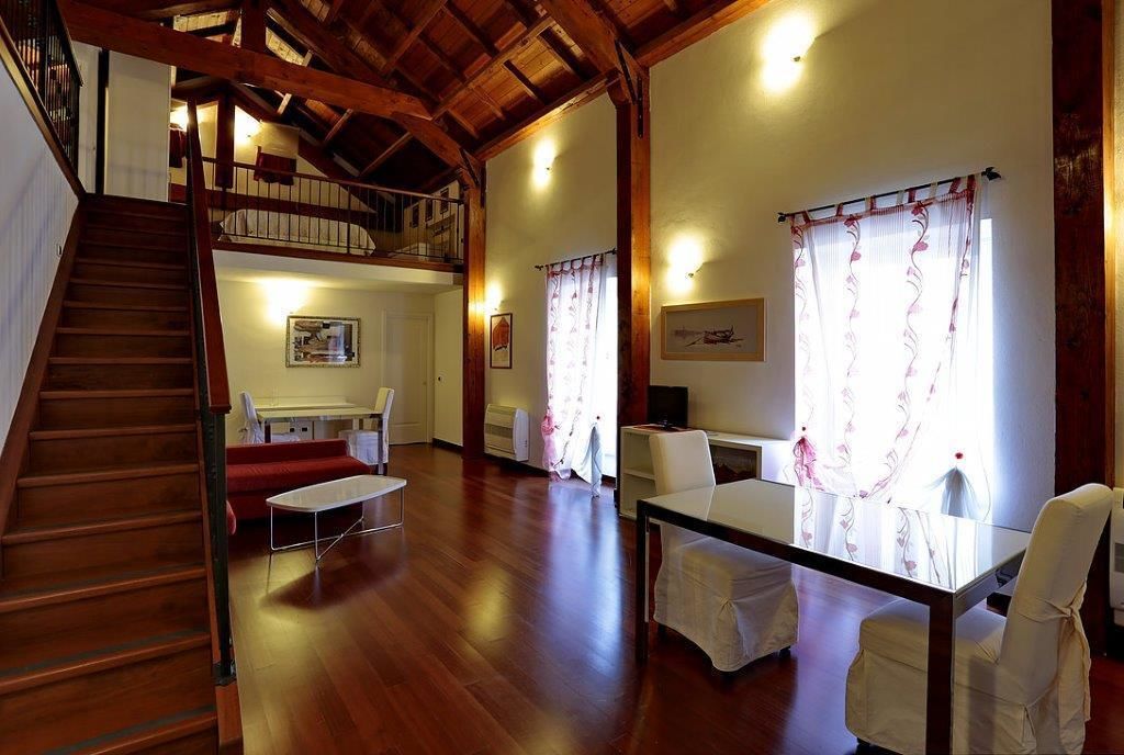 Un amplio salón con una escalera de madera, una mesa de comedor y un sofá.