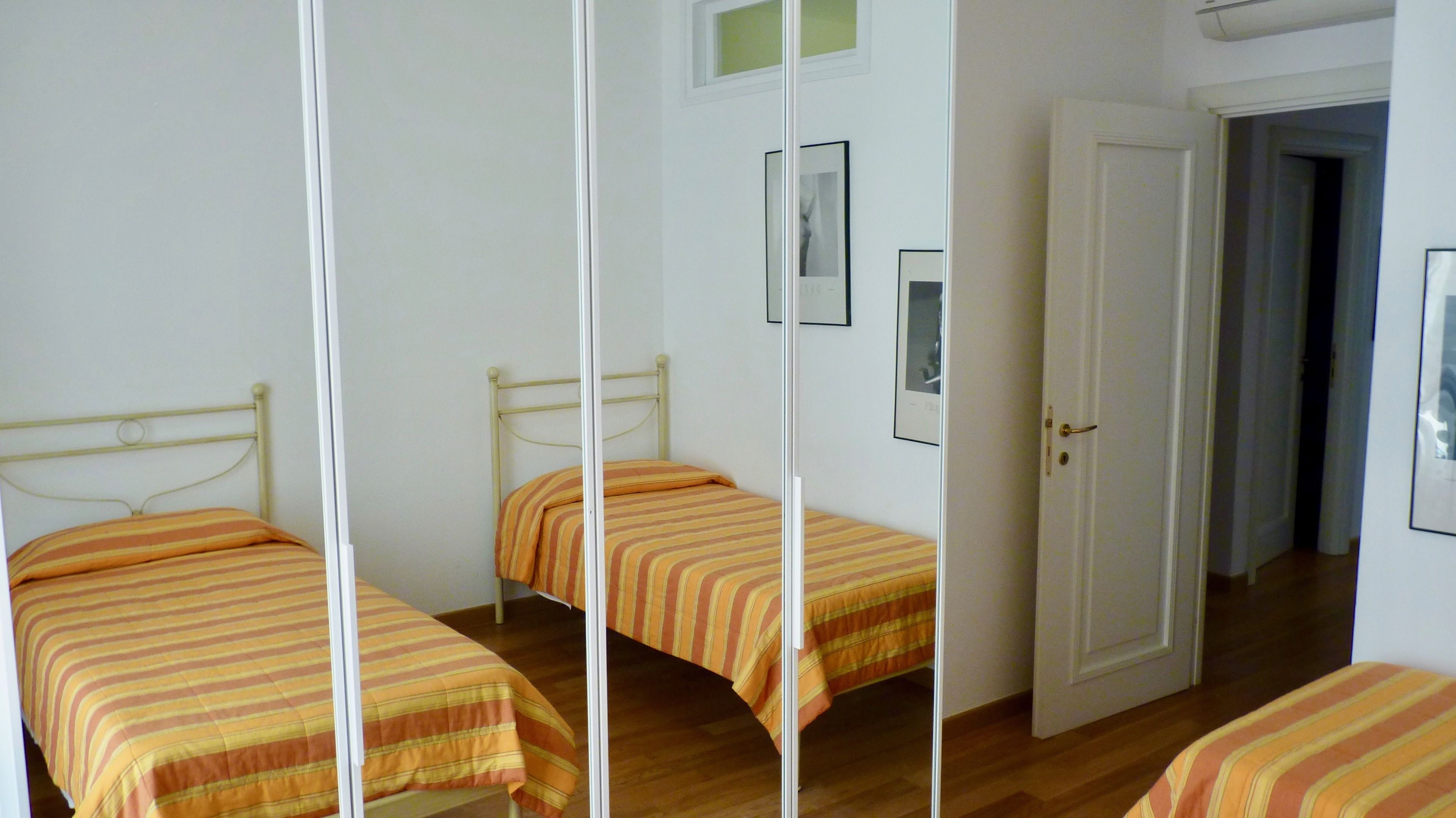 Une chambre avec deux lits simples, chacun doté de draps à rayures, une porte blanche et un tableau encadré au mur.