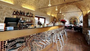 Zona de bar con techo de piedra, taburetes y una variedad de botellas en estanterías.