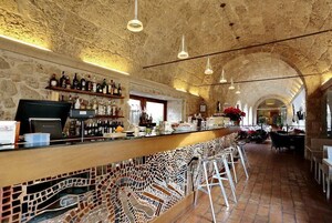 Un'area bar con soffitto in pietra, sgabelli da bar e varie bottiglie sugli scaffali.