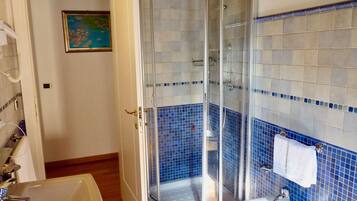Baño con ducha envuelta en vidrio, lavamanos y retrete.
