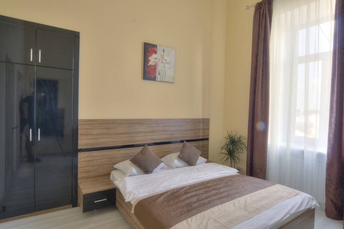 A bedroom with a bed, a wardrobe, a painting, and a window with curtains.