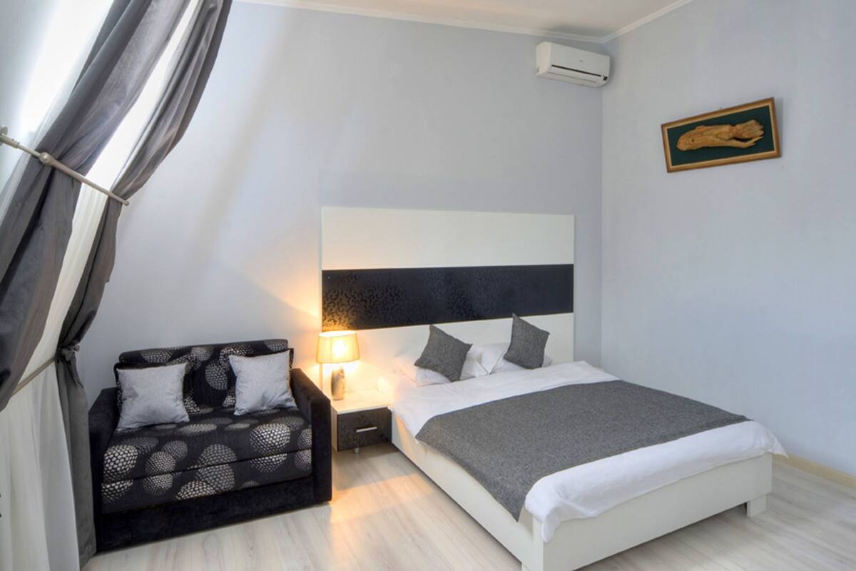 A bedroom with a bed, a nightstand, a sofa, a lamp, and a wall-mounted air conditioner.