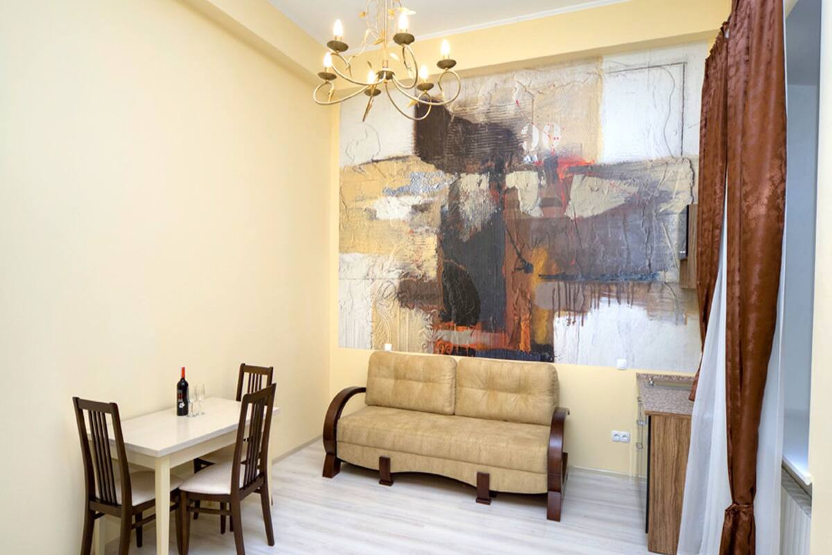 A dining area with a table and chairs, a sofa, a chandelier, and a large abstract painting on the wall.