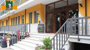 Hotel 3 Monti features a modern exterior with a bright entrance and a balcony with potted plants.