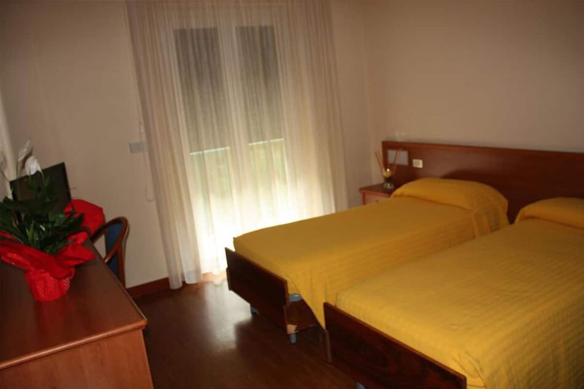 A hotel room with a wooden bed, a bedside table, a chair, and a window with curtains.
