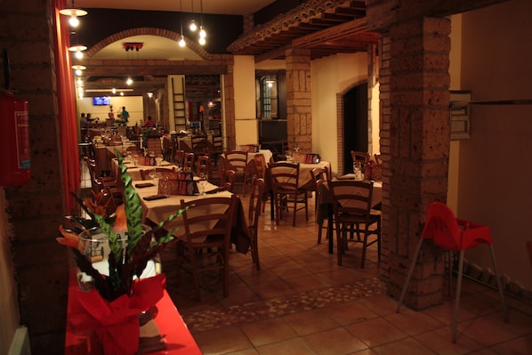 A restaurant with multiple tables and chairs, brick walls, and a tiled floor.