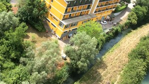 A multi-story yellow building with a green roof, surrounded by dense greenery and a river. - Hotel Tre Monti (Popoli)