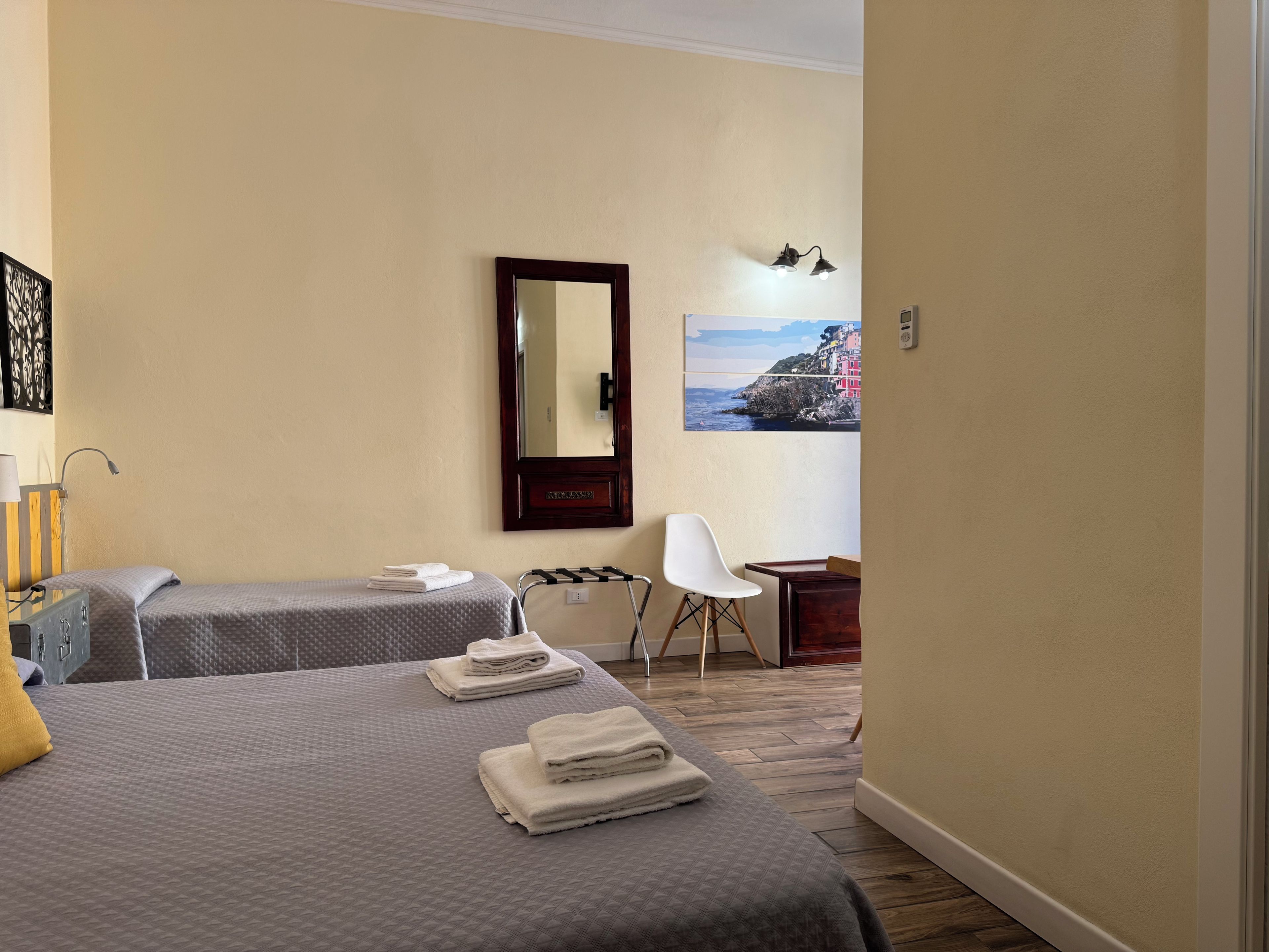 Quarto de hotel com duas camas, uma escrivaninha, uma cadeira, um espelho e um quadro na parede.