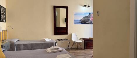 Quarto de hotel com duas camas, uma escrivaninha, uma cadeira, um espelho e um quadro na parede.
