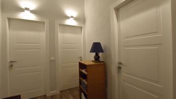 Ein Flur mit weißen Türen, einem hölzernen Regal mit einer Lampe und einem Holzboden.
