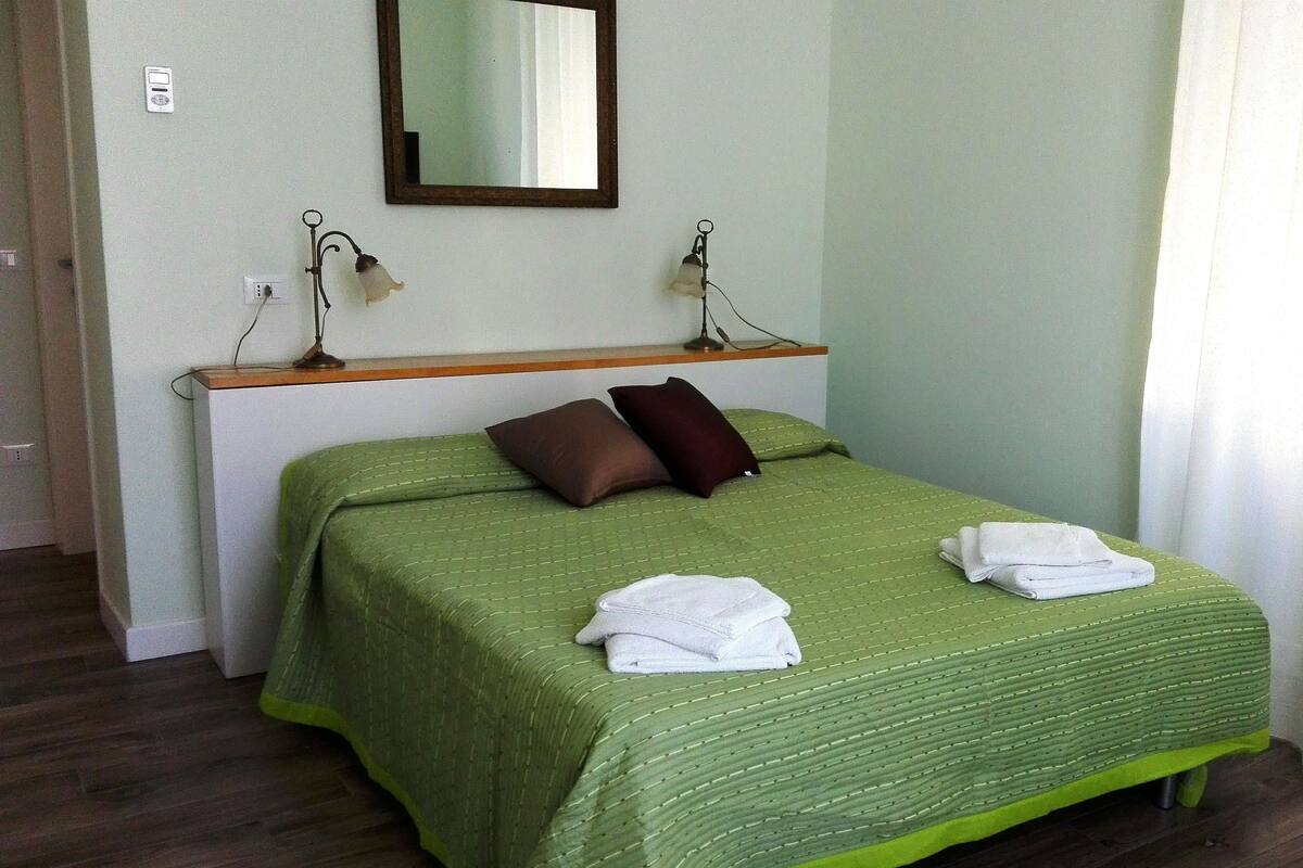 Ein ordentlich bezogenes Bett mit grüner Bettwäsche, zwei Kissen und zwei gefalteten Handtüchern.