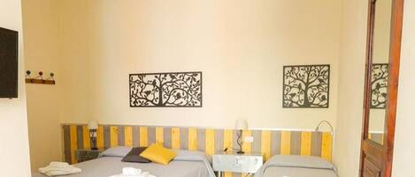 A hotel room with two beds, a desk, chairs, and artwork on the walls.