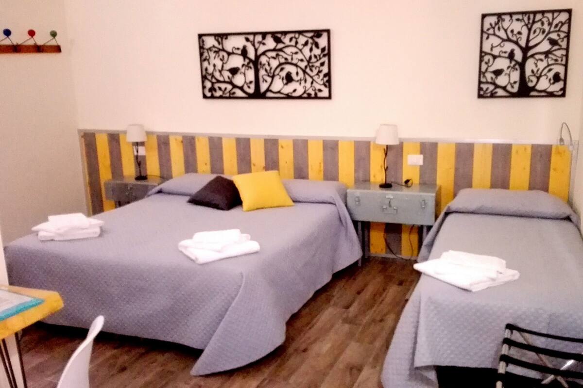 Ein Zimmer mit zwei Einzelbetten, jeweils mit Kissen und einem gefalteten Handtuch. Über den Betten befinden sich jeweils eine Wandleuchte und ein gerahmtes Kunstwerk.