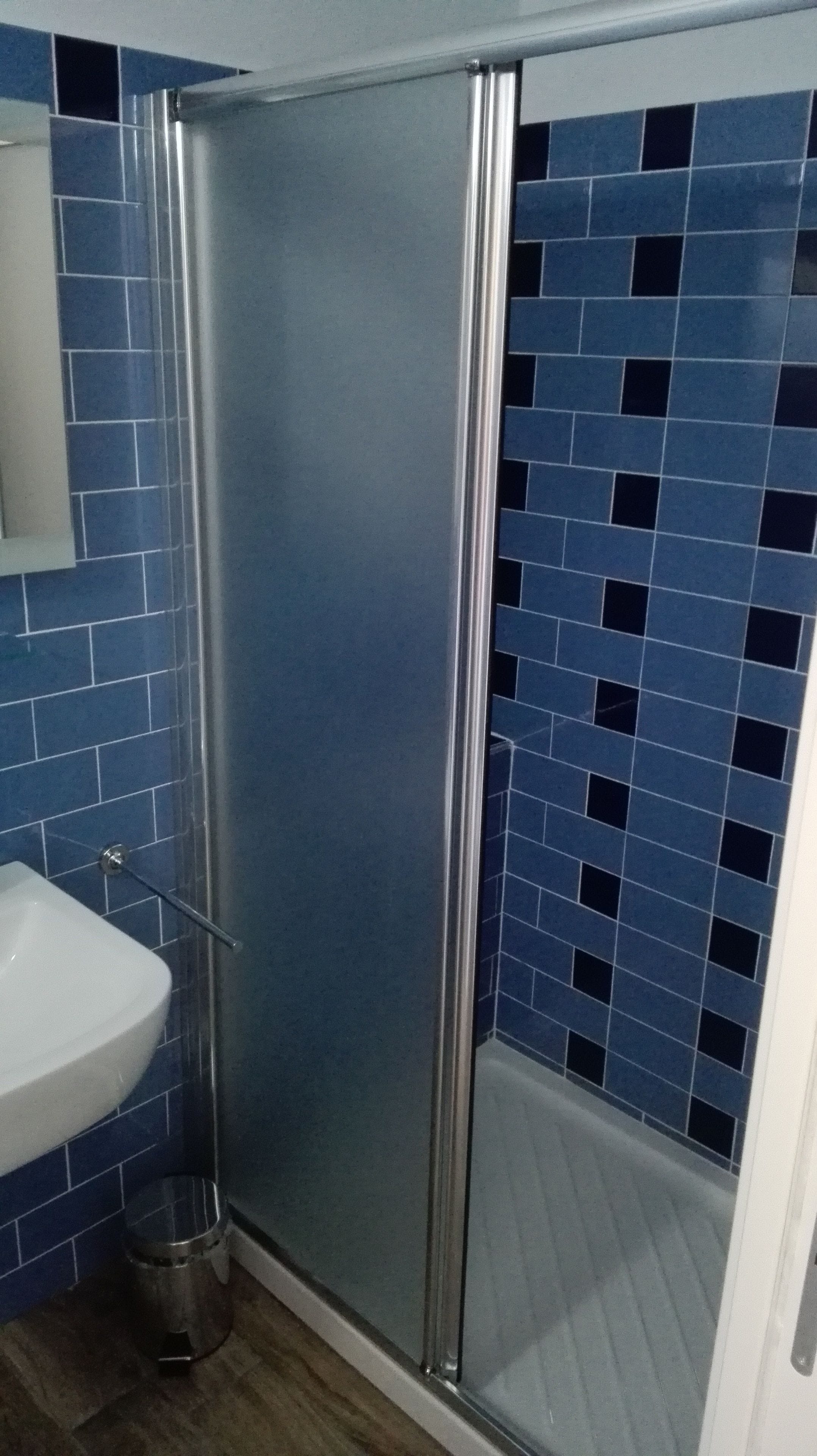 Une salle de bain avec un espace douche, un lavabo et des murs recouverts de carreaux bleus.