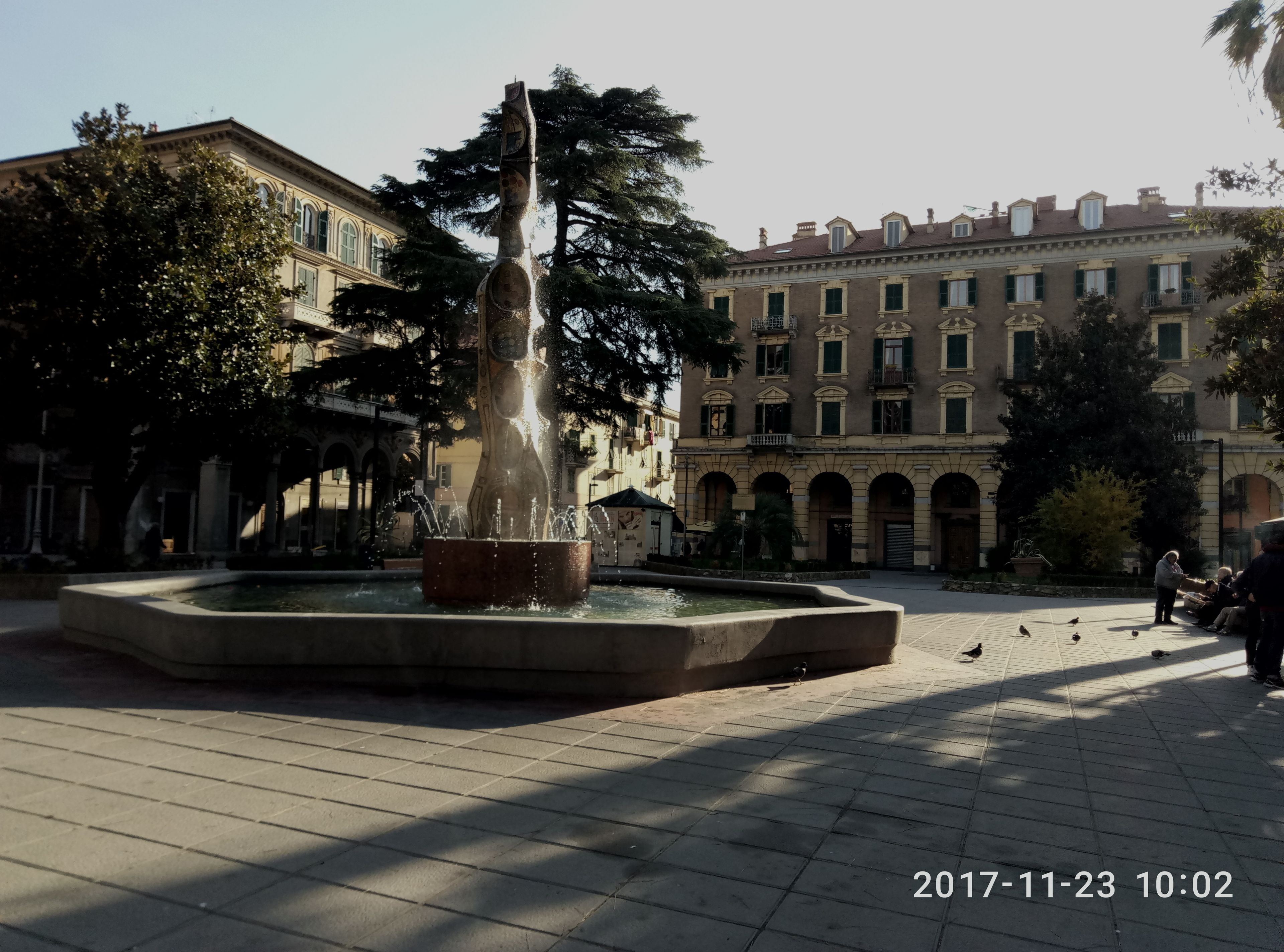 Ein Brunnen auf einem Platz, im Hintergrund ein Gebäude.