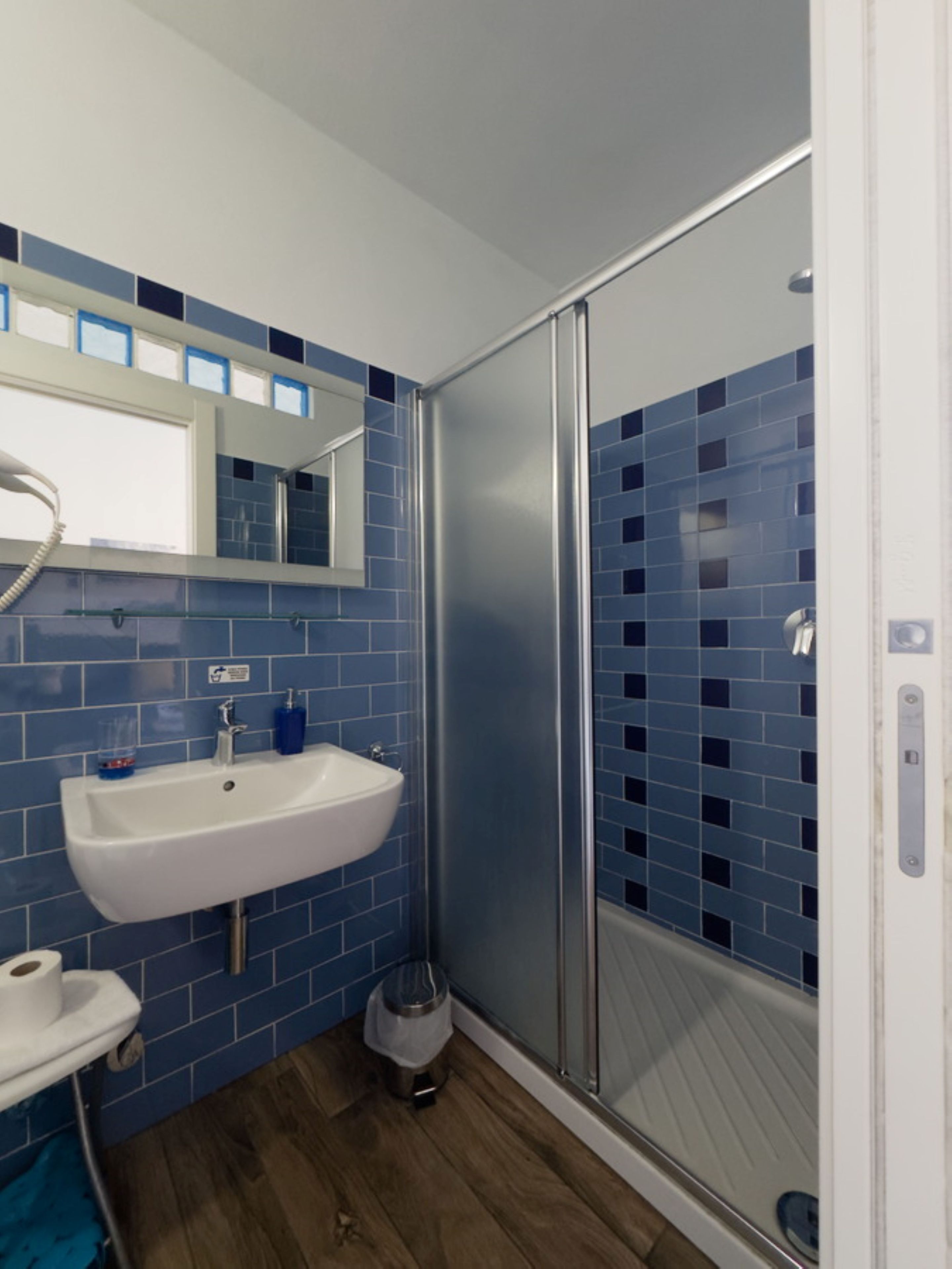A bathroom with a white sink, blue-tiled walls, and a glass shower enclosure.