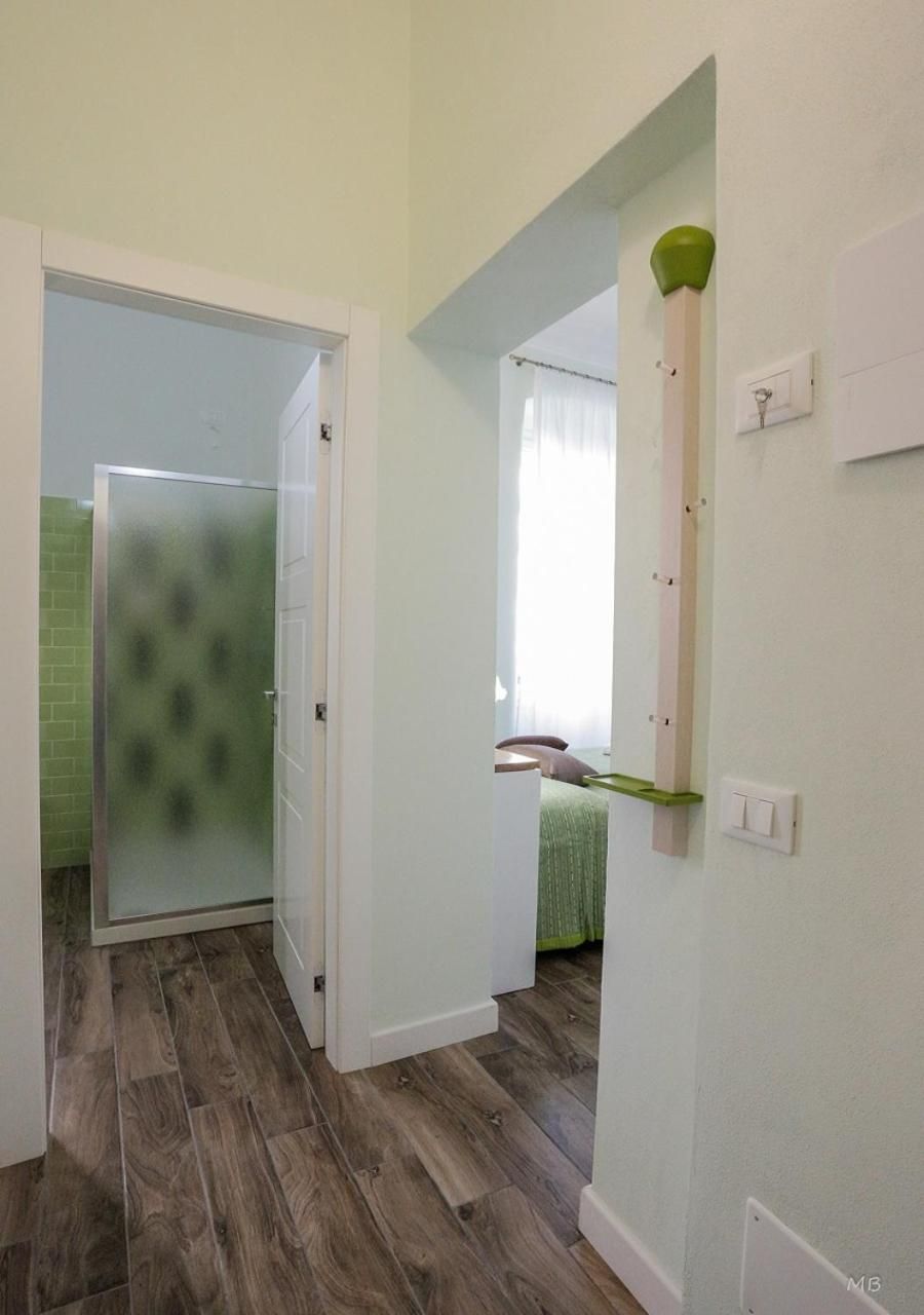 A hallway with a wooden floor, a frosted glass door, a bed with a green bedspread, and a wall-mounted light fixture.