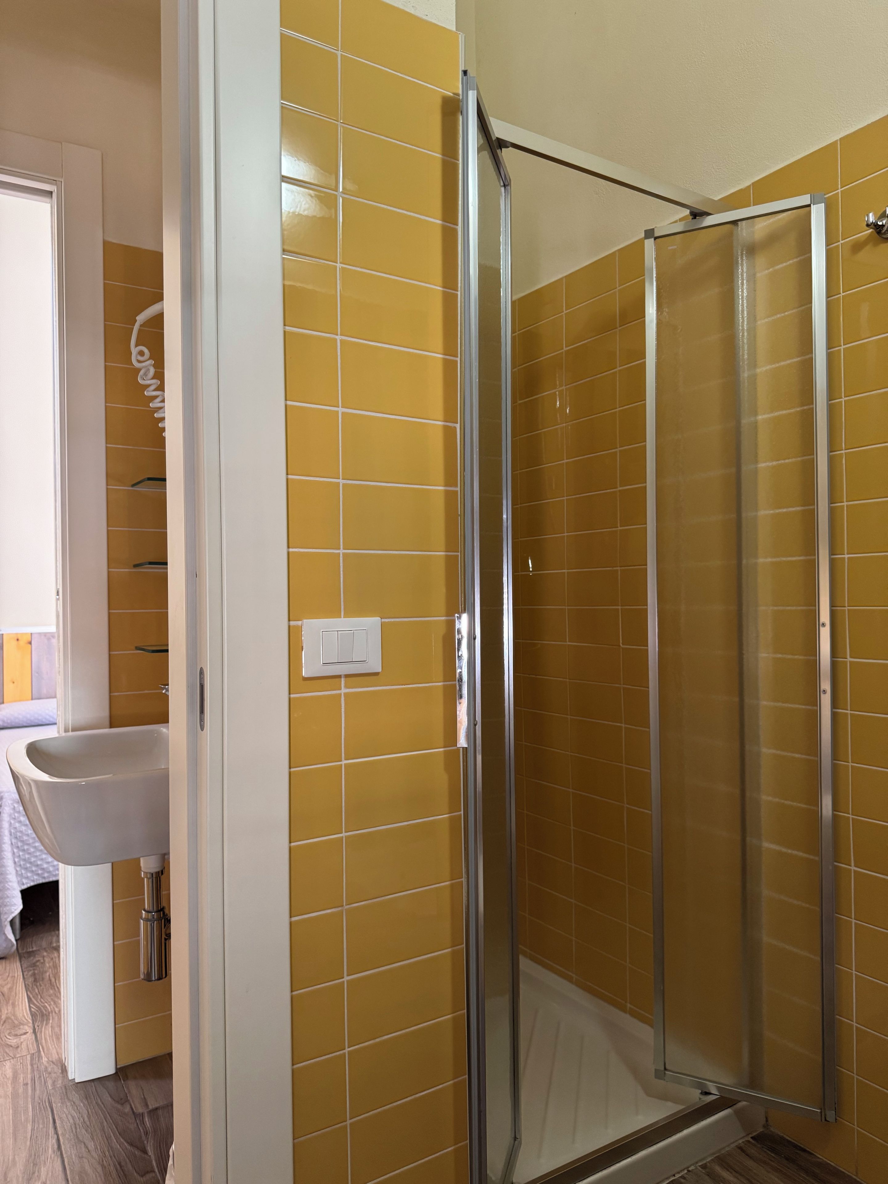 Un baño con paredes de azulejos amarillos, un lavabo blanco y una cabina de ducha de vidrio.