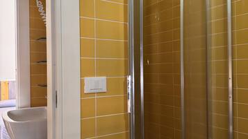 A bathroom with yellow tiled walls, a white sink, and a glass shower enclosure.