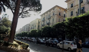 Una hilera de edificios clásicos de estilo europeo, con fachadas uniformes, coches estacionados en la calle y un peatón que pasa.