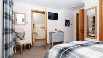 Ein Schlafzimmer mit Bett, Kommode, Stuhl, Spiegel und Fernseher.