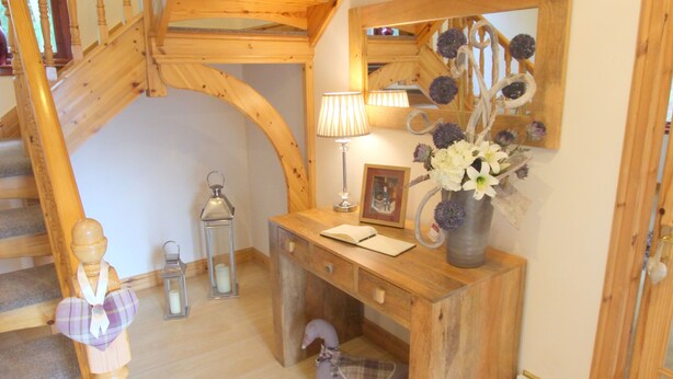 Un escalier en bois avec un plafond incurvé, un bureau en bois orné d’un vase de fleurs et un miroir accroché au mur.