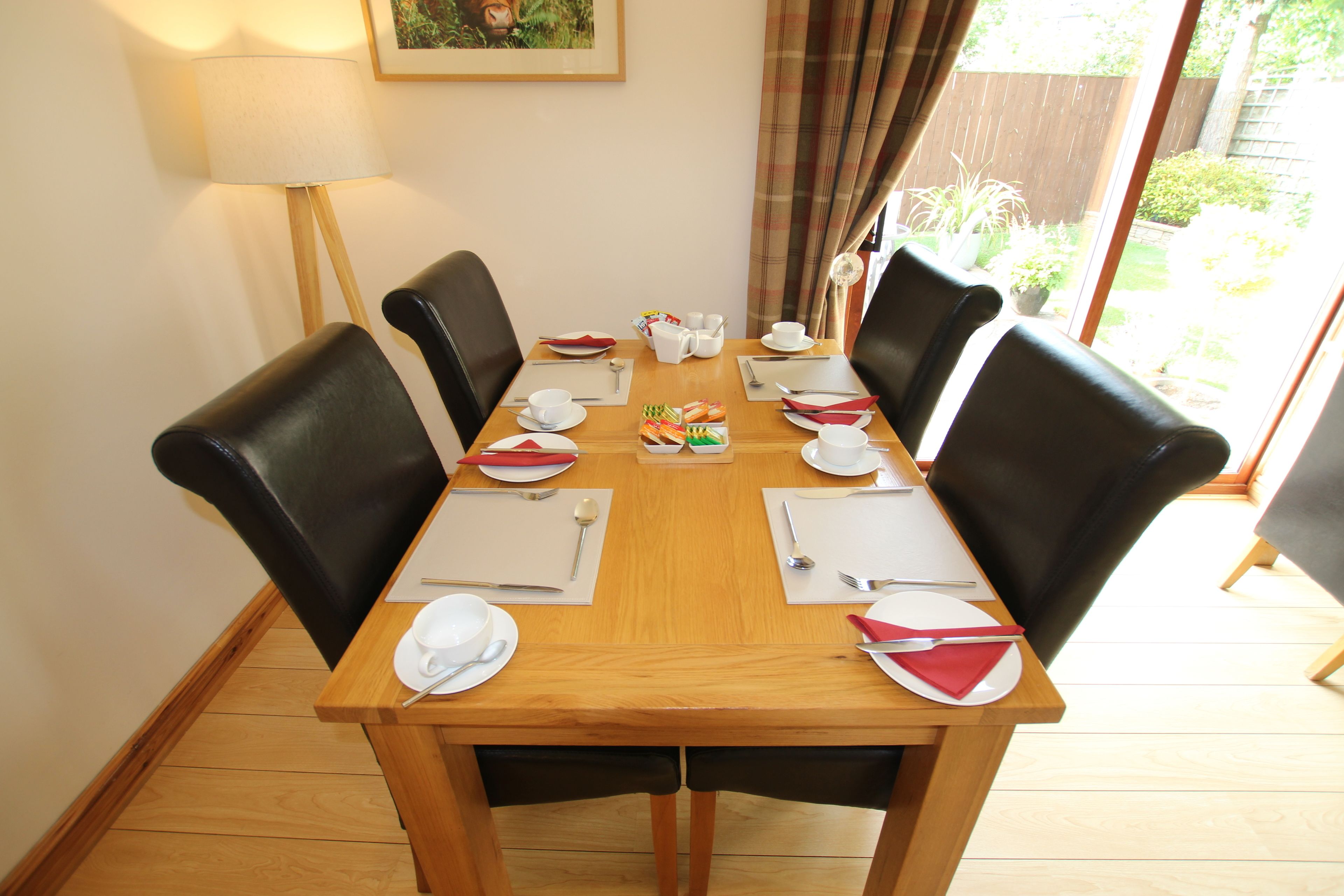 Taula de dinar preparada per a sis persones, amb cadires negres, plats blancs i coberts.