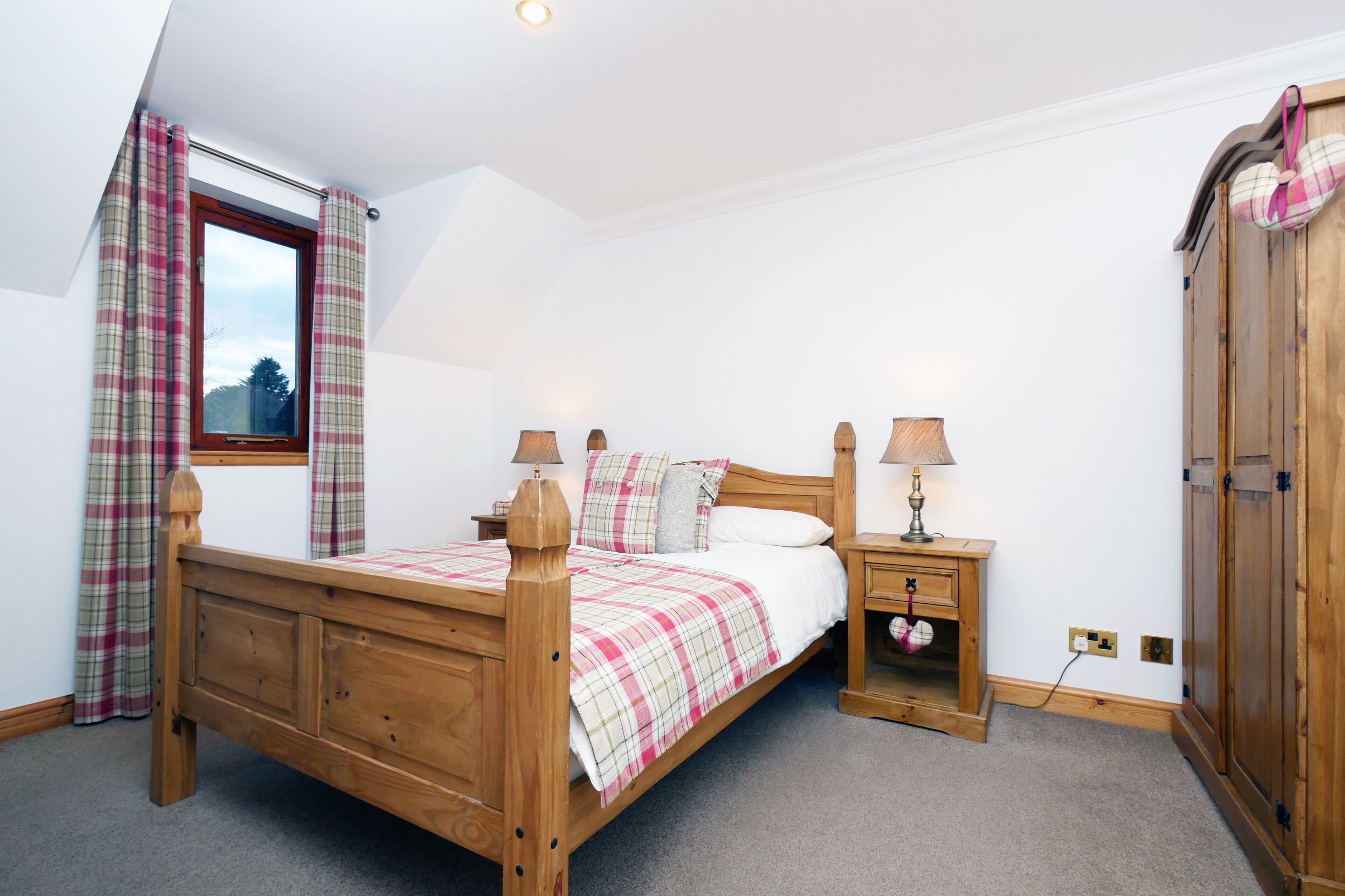 A bedroom with a wooden bed, a nightstand, a wardrobe, and a window with plaid curtains.