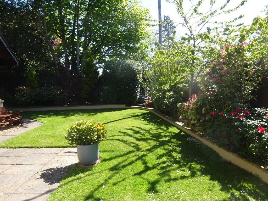 A well-maintained garden with a lawn, a potted plant, and a variety of shrubs and flowers.