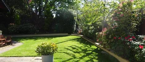 A well-maintained garden with a lawn, a potted plant, and a variety of shrubs and flowers.