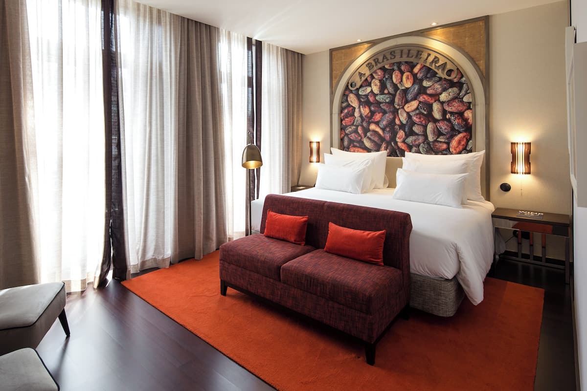 Habitación de hotel con una cama grande, un sofá rojo, un escritorio y una pared con un mural de granos de café.