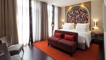 Habitación de hotel con una cama grande, un sofá rojo, un escritorio y una pared con un mural de granos de café.